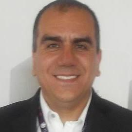 The face of Ernesto smiling for the camera. He is wearing a smart shirt and jacket.