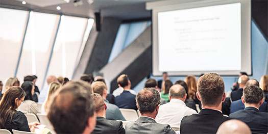 Attendees of mixed genders watching a presentation at a conference.