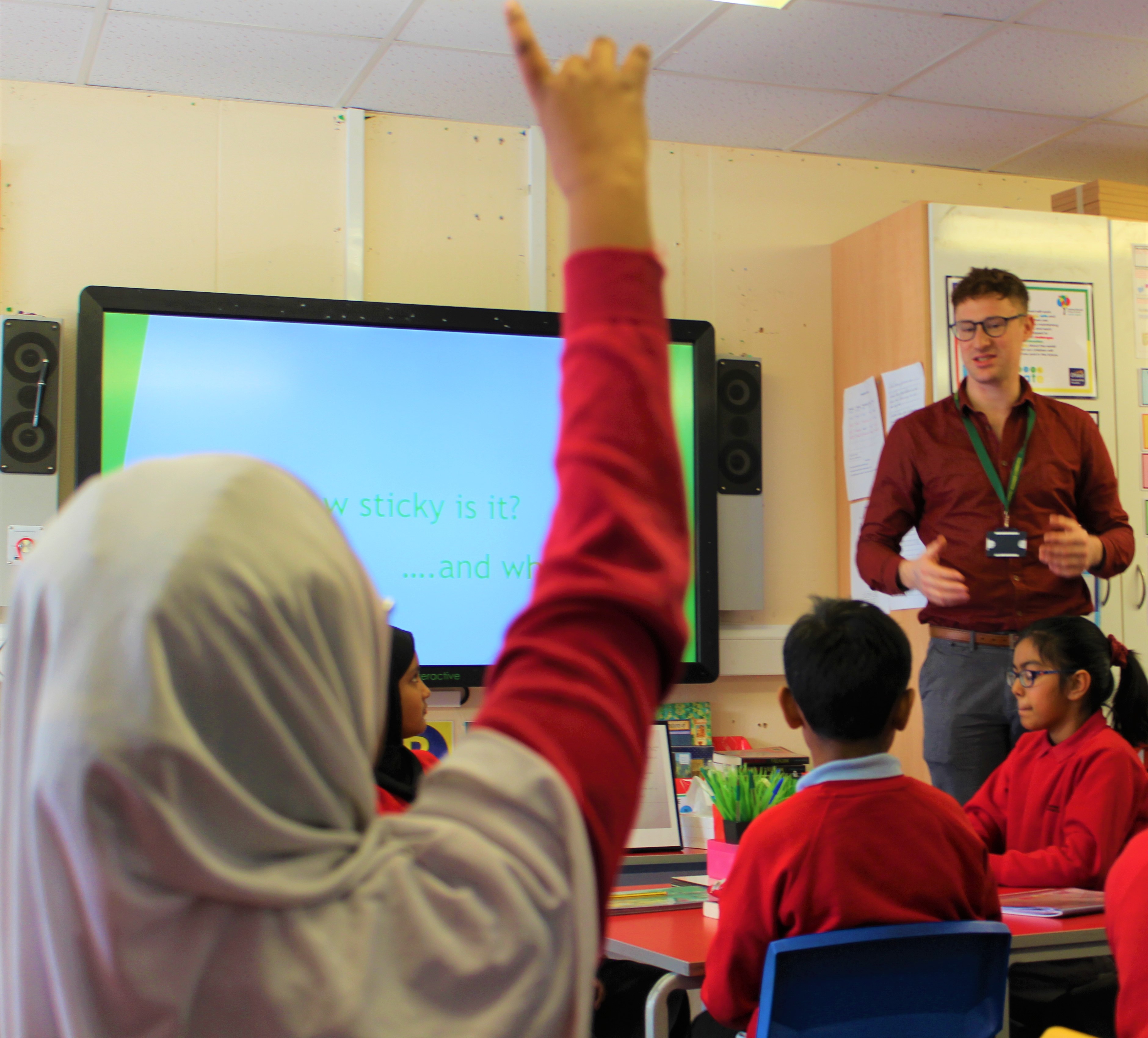 A school child with their hand up waiting to answer a question