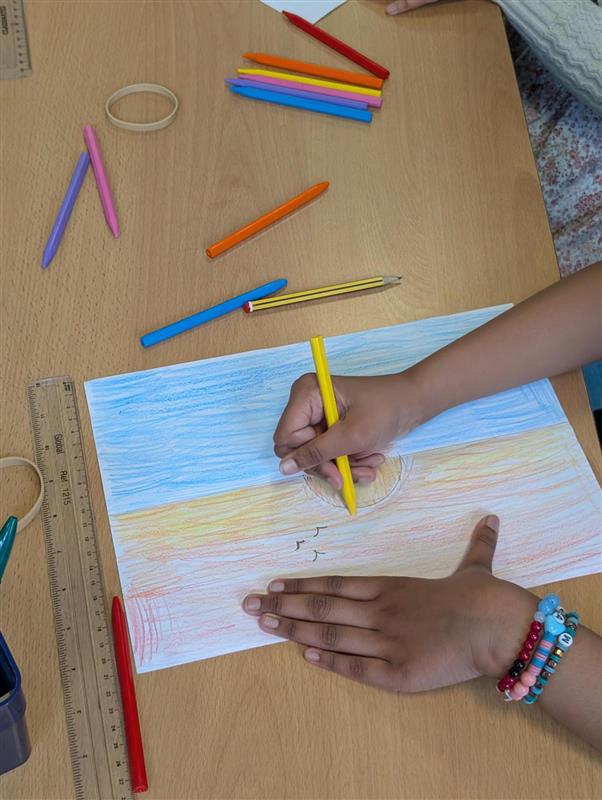 School pupil drawing a sunset with colourful crayons