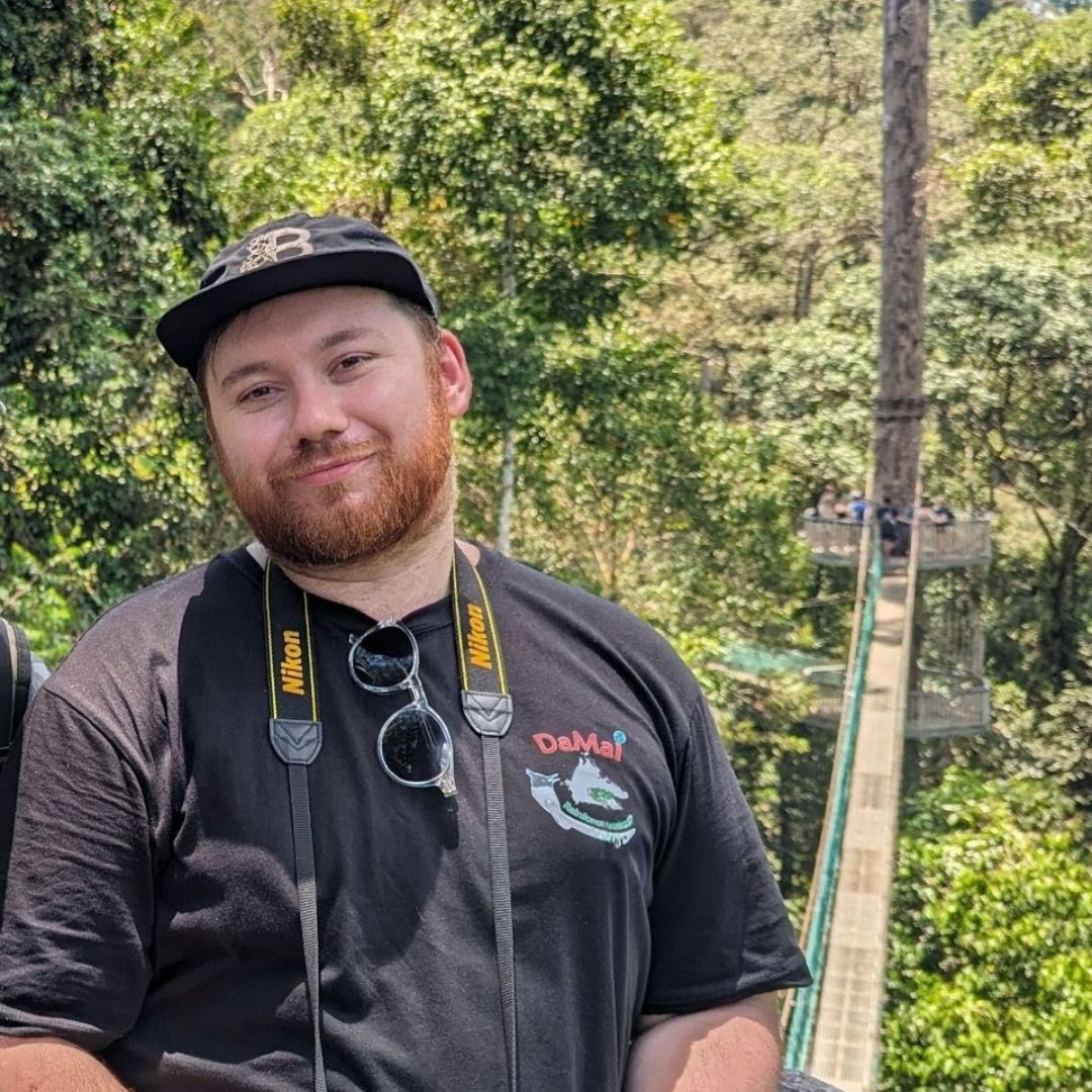 Matthew Hulse smiling at the camera with a rainforest background