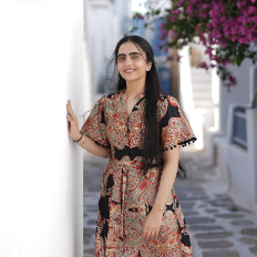 Photo of Farah smiling and looking towards the camera within a cobbled street with flowers in the background