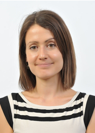 Headshot . Looking at the camera wearing a white and black top. Behind is a white background.