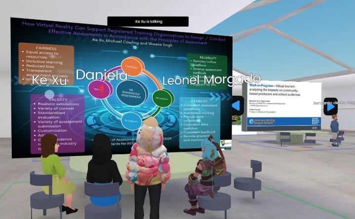 Virtual and animated image. Appears to be four avatars looking at a screen. Three seated. There is another screen in the background. It is a large open space.